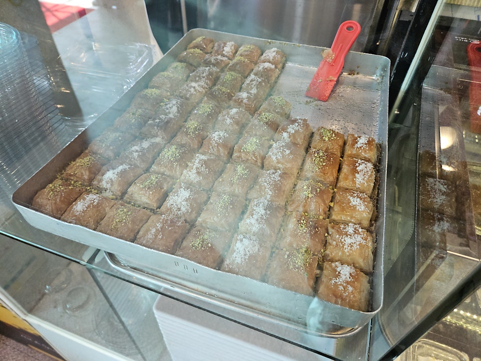 tpasa는 직원이 꼬치를 돌려 굽는 오픈 키친과 이스켄데르 케밥 광고판을 함께 찍었고, 진열장 속 바클라바 한 판도 따로 담았다.