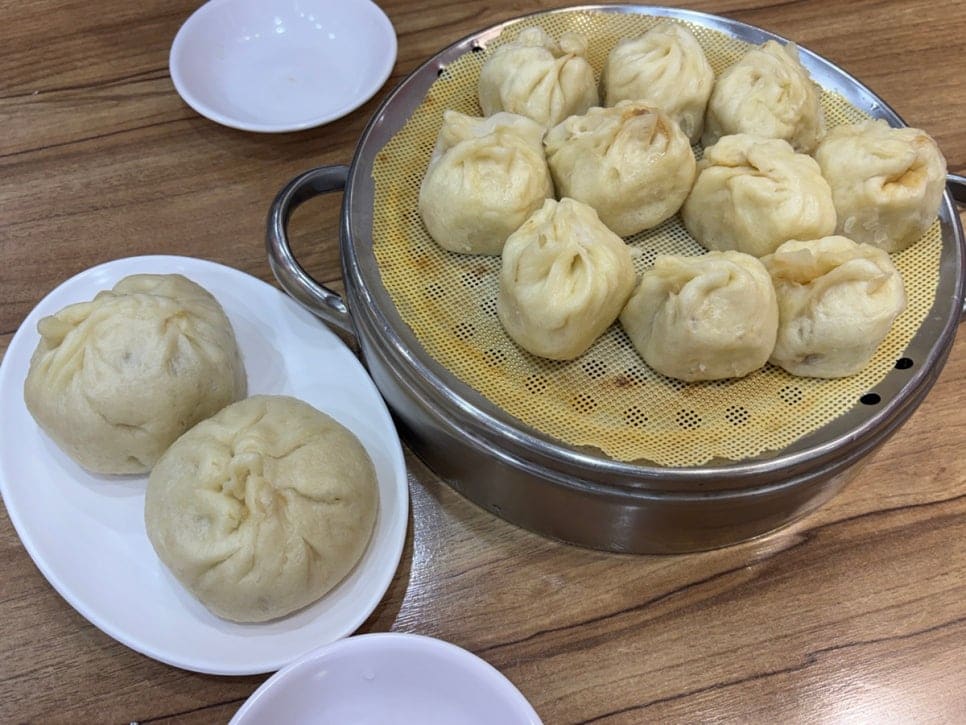 fnrakf97은 찜통에서 막 꺼낸 작은 만두와 왕만두, 그리고 셀프로 덜어온 무생채 한 접시를 찍었다. 소스 그릇은 각자 입맛대로 채워 넣게 비워져 있었다.