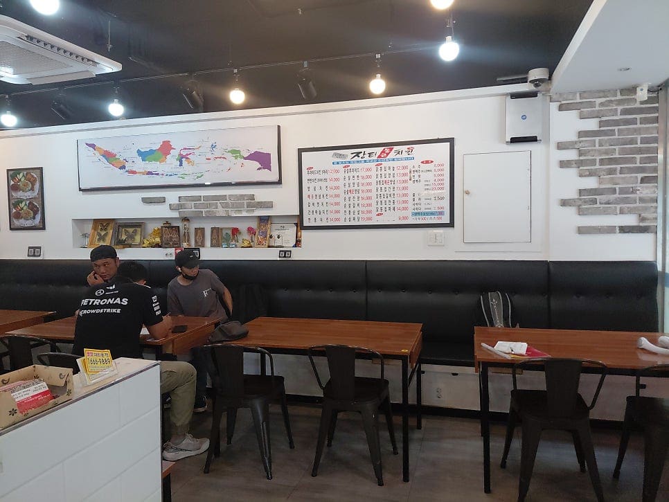 상어밥(smarkshark)은 인도네시아 지도 액자와 '장터통큰치킨' 메뉴판이 나란히 걸린 벽, 그리고 손님들이 앉은 테이블과 음료 냉장고가 보이는 매장 안쪽을 찍었다.