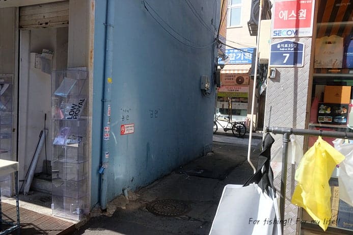 간판이 빼곡히 걸린 좁은 골목과, 벽면 가득 물건이 쌓인 안쪽 통로입니다. 좁아지는 보행 폭을 실감할 수 있는 장면입니다.