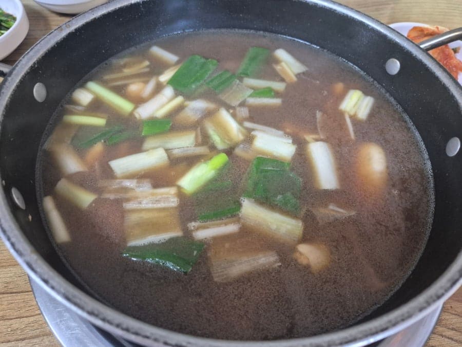 877번째 포스팅을 이 집으로 채운 foodprintblog가 남긴 사진입니다. 진한 갈색의 한방 육수가 냄비 안에서 끓어오르고, 대파와 부추가 그 속에 잠겨 있습니다.