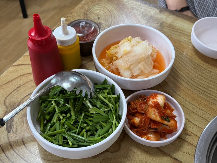 같은 사람이 남긴 밑반찬 사진입니다. 부추와 물김치, 배추김치가 소스병과 함께 상에 올라 있습니다.