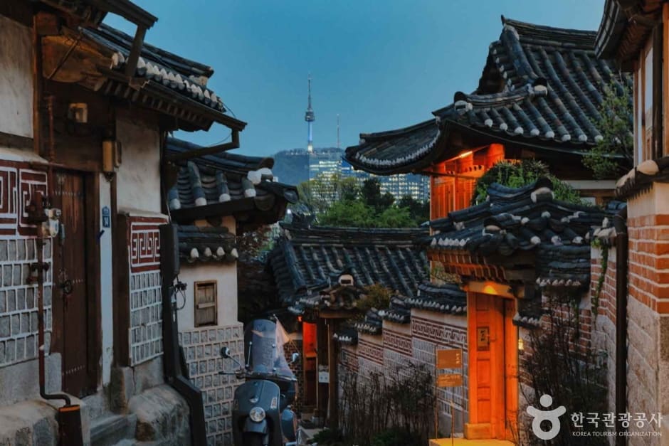 왼쪽은 낮 시간대 계동길 골목. 한옥 기와지붕 사이 좁은 통로를 관광객들이 걷고 있고 멀리 도심 빌딩이 겹쳐 보인다. 오른쪽은 해질 무렵 같은 골목으로,