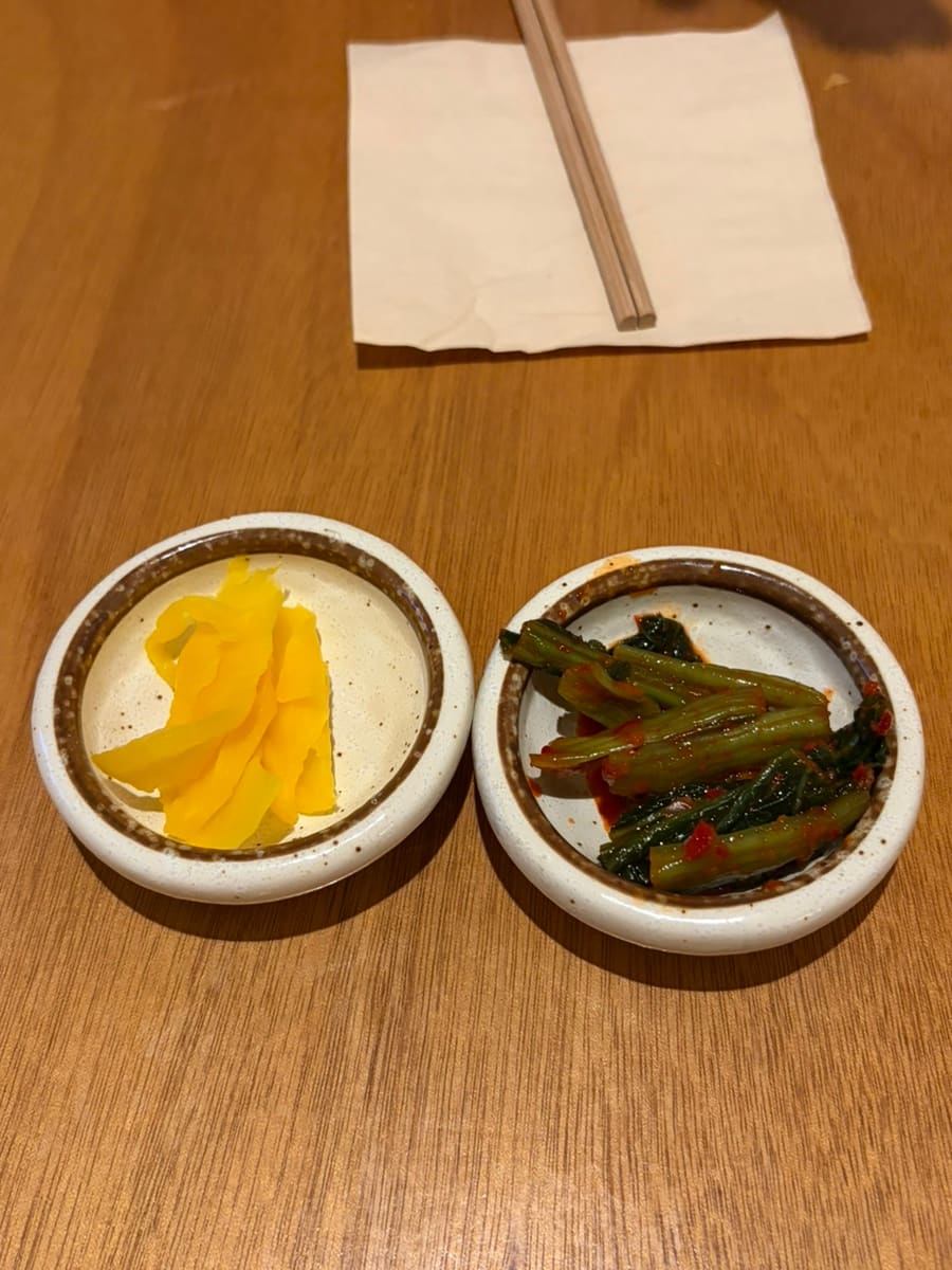 기본으로 나온 밑반찬입니다. 단무지와 매콤하게 무친 초록 채소가 작은 그릇에 나뉘어 담겨 있습니다.