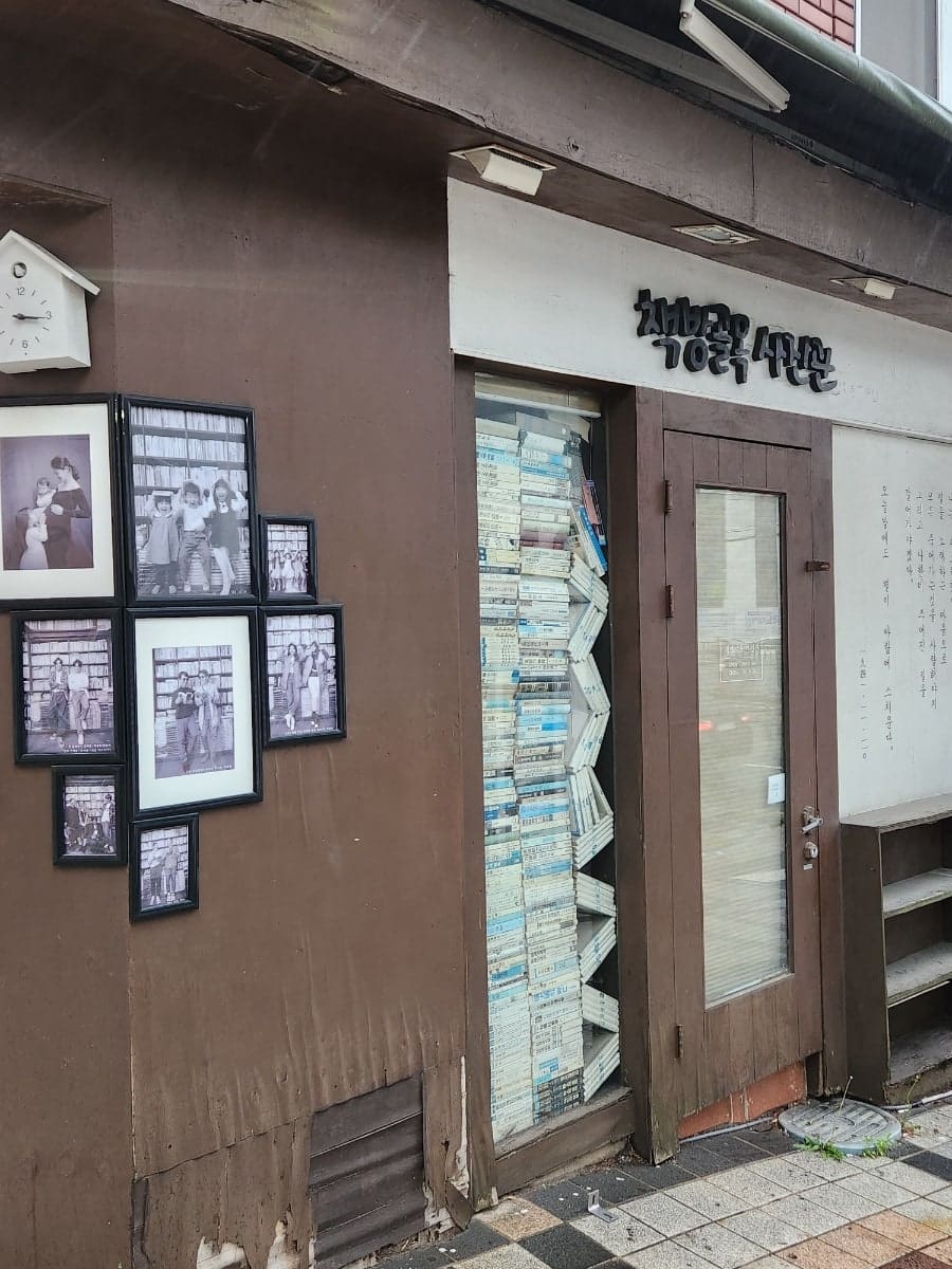 가족사진이 걸린 책방 외벽과, 비에 젖은 채 셔터가 늘어선 골목 통로다. 사람이 없는 아침, 젖은 바닥 위로 정적이 내려앉는다.