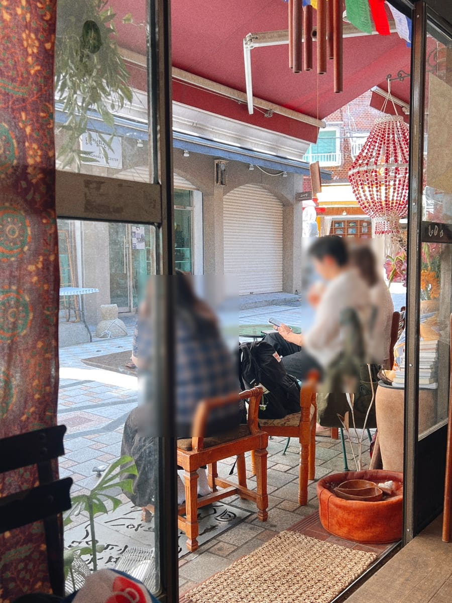 빛바랜 나무 테이블 위에 놓인 생화 한 다발과, 만트라 깃발과 풍경이 걸린 처마 아래 테라스 자리를 이 블로거가 남겼습니다.