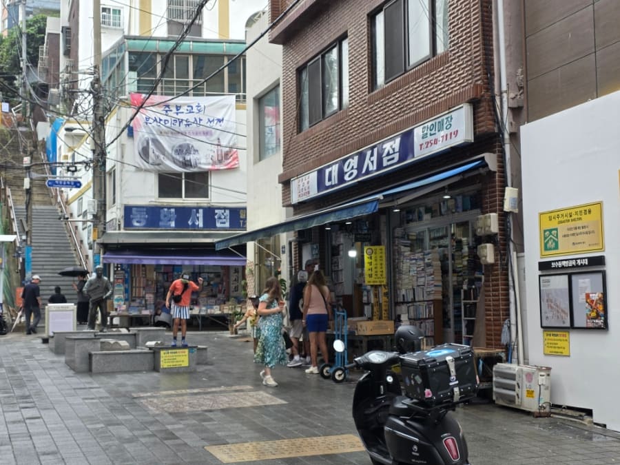 책방골목 어린이 도서관 방향을 가리키는 표지판과, 대영서점 간판 아래로 사람들이 오가는 골목 초입이다. 헌책방은 지금도 이 자리에서 문을 연다.