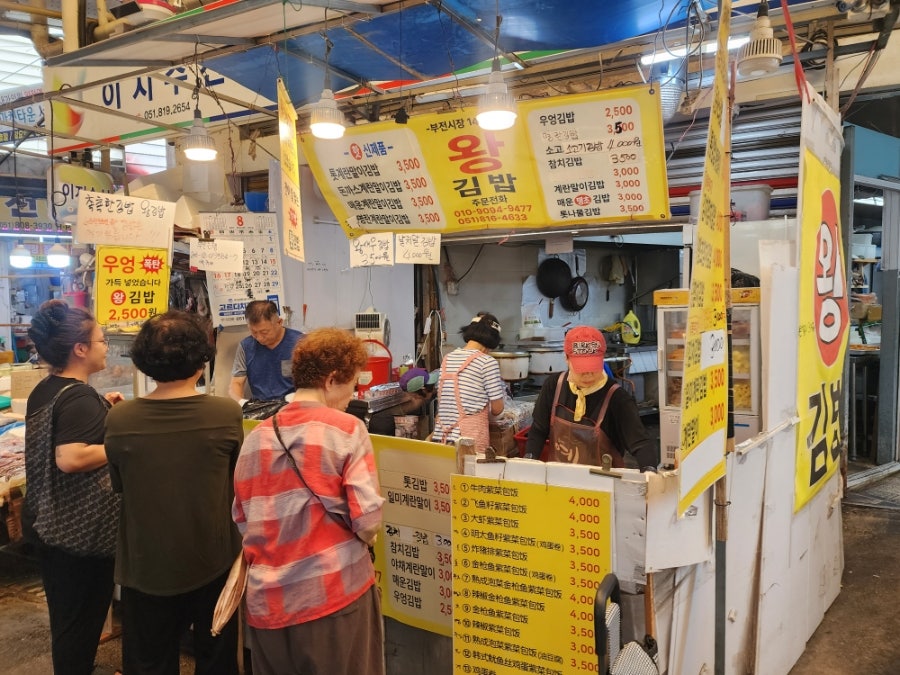 77soul이 담은 김밥 좌판들입니다. '왕김밥' 앞에는 손님들이 줄지어 서 있고, 몇 걸음 옆 '명란김밥' 간판 아래로도 또 다른 줄이 이어집니다.