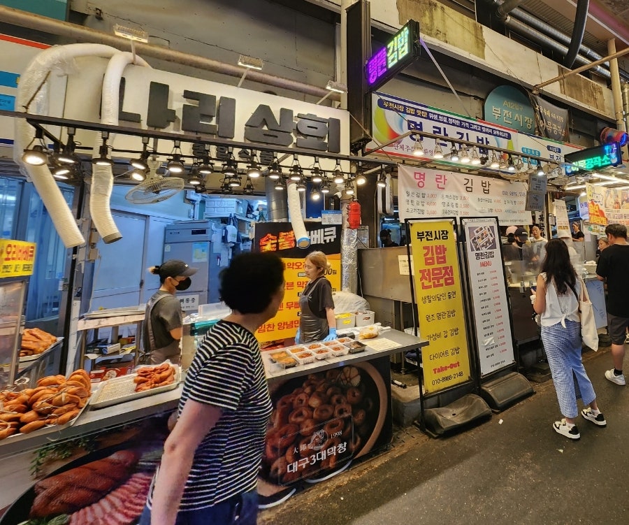 77soul이 담은 김밥 좌판들입니다. '왕김밥' 앞에는 손님들이 줄지어 서 있고, 몇 걸음 옆 '명란김밥' 간판 아래로도 또 다른 줄이 이어집니다.