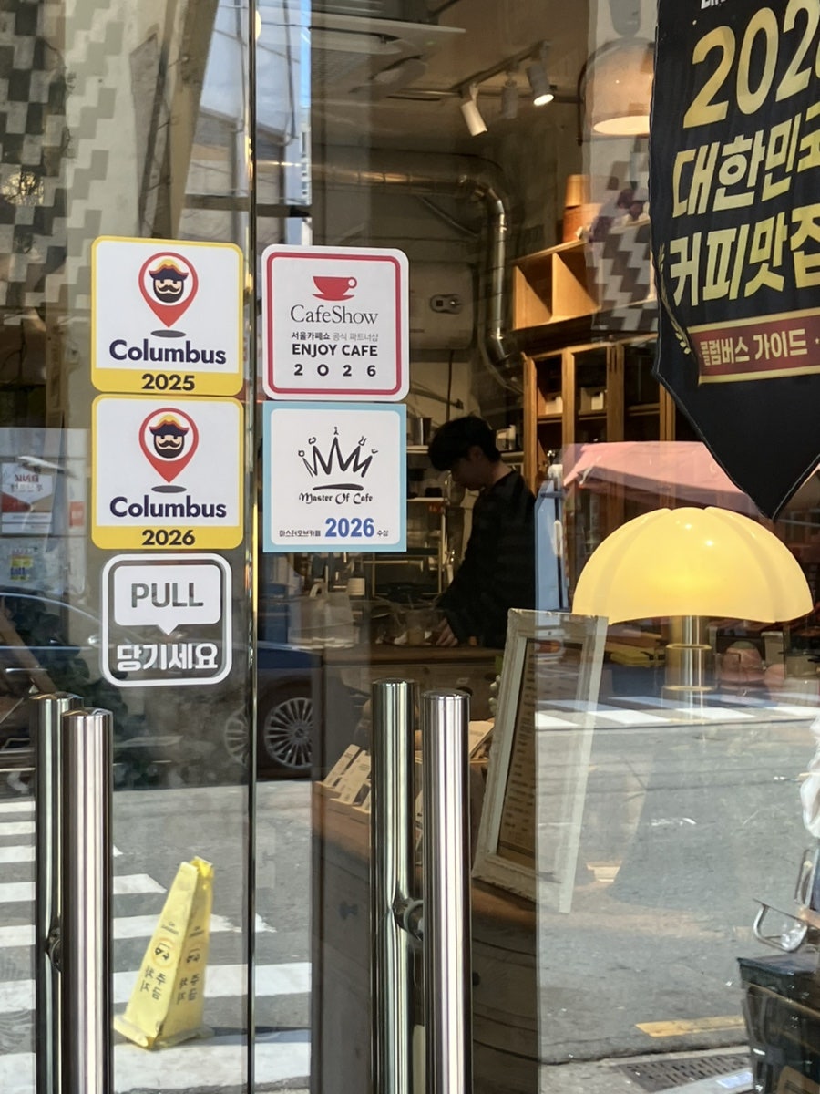 take_list가 담은 가게 안쪽입니다. 출입문에는 'Columbus' '마스터오브커피' 같은 라떼아트 대회 수상 스티커가 나란히 붙어 있고,