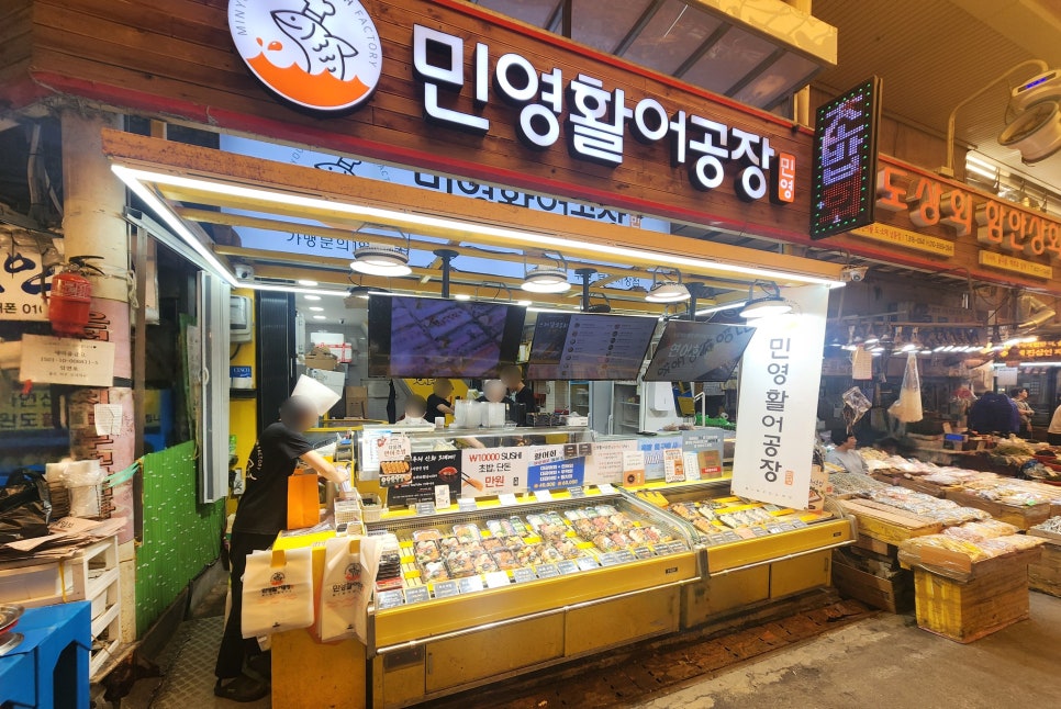 leesunyou가 저녁 무렵 담은 사진입니다. 불을 환하게 밝힌 가게 전경과, 광어·연어·우럭·모둠초밥이 가격표와 함께 진열대 가득 늘어선 모습이 나란합니다.