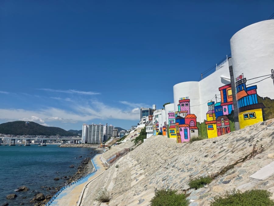 1217peace 님이 해안 산책로에서 올려다본 벽화입니다. 색을 입은 집 그림이 실제 마을 지붕선과 겹쳐 보이는 자리로,