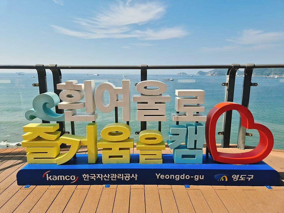 jheasy1405 님이 남긴 암벽 사이 출렁다리와, kikihera 님이 남긴 흰여울로 조형물입니다. 흔들리는 다리를 건너는 사람들 뒤로 도심 스카이라인이 멀리 걸립니다.