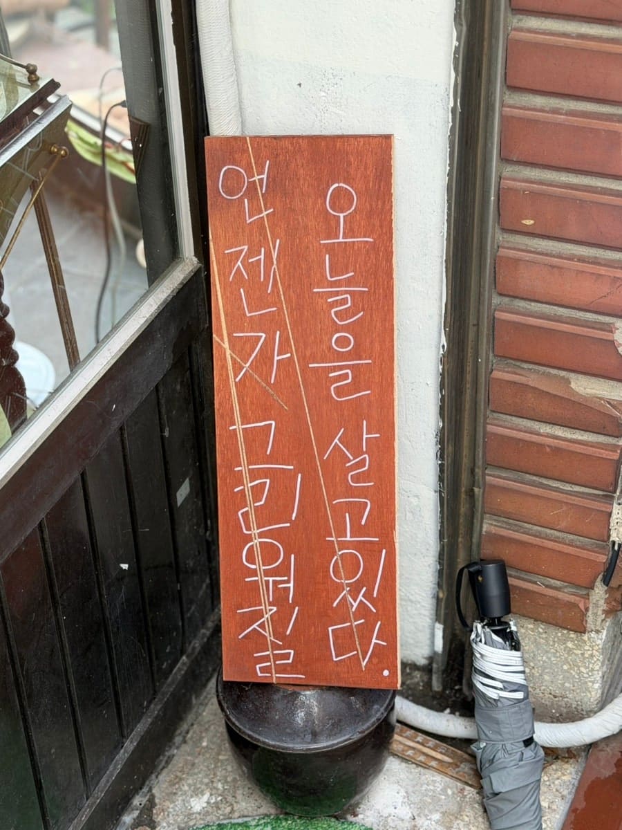 카페 입구 옆 낡은 벽에 손글씨로 적힌 쪽지를 발견한 블로거는 그 장면을 가까이서 찍어 남겼습니다. 낡은 벽돌과 벗겨진 페인트, 그 위에 붙은 '기똥찬 하루 보내세요'라는 글씨,