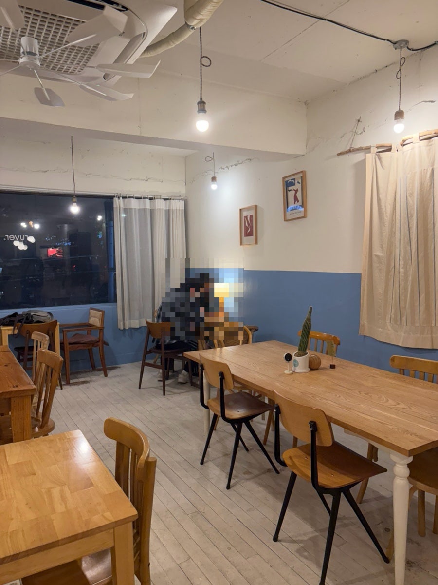 rkawk0904_이 담은 실내입니다. 파란 반벽 아래 원목 테이블과 의자가 놓여 있었고, 다른 한쪽 원목 수납장 위에는 머그잔과 화병들,