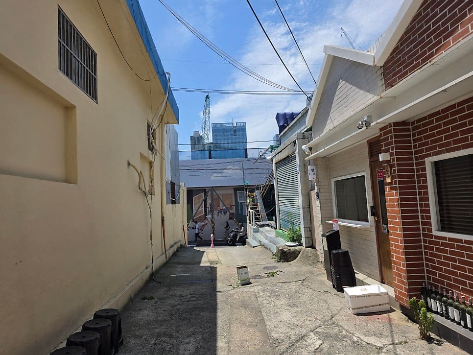 이 골목을 지나던 블로거는 좁은 뒷골목 사진과 함께, 낮은 벽돌 건물들 사이로 올려다보이는 공사 중인 고층 건물의 크레인을 같은 프레임에 담았습니다.