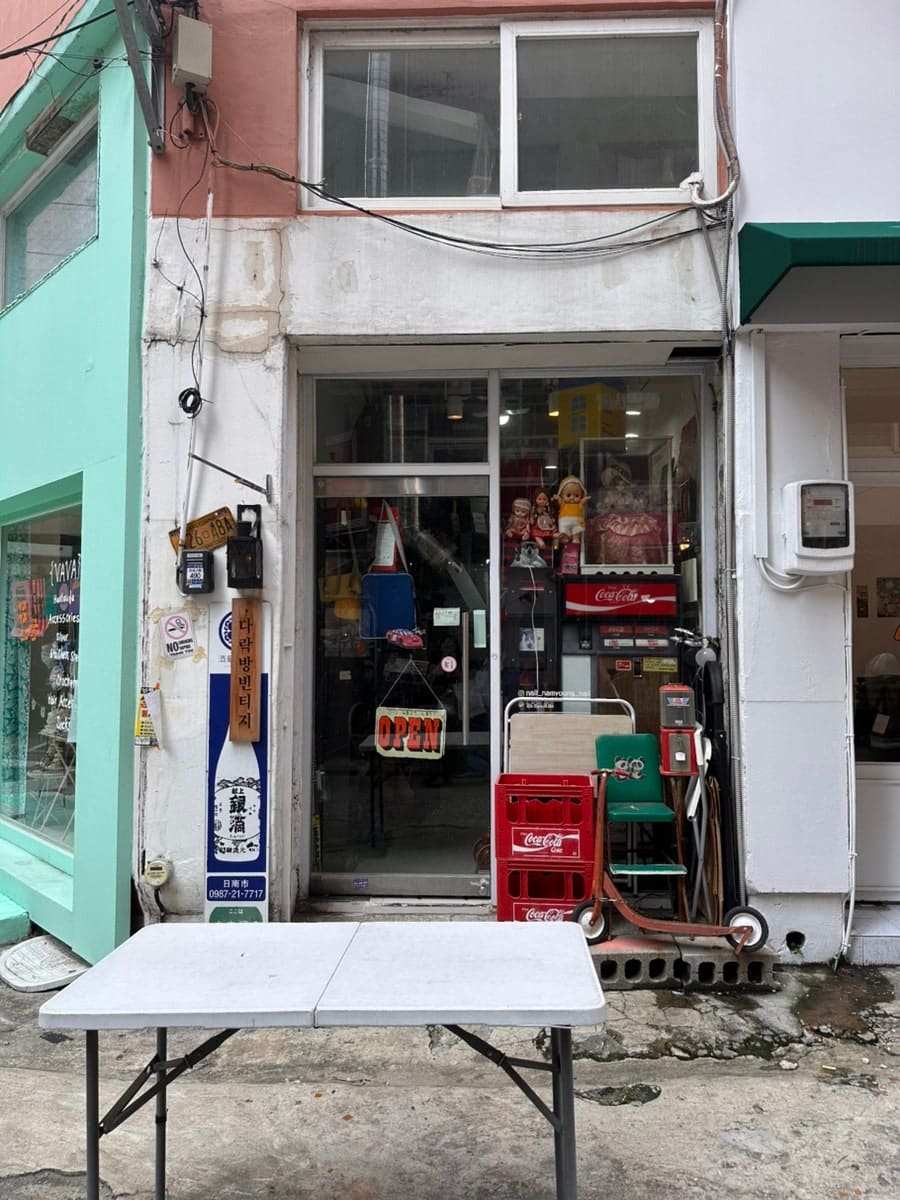 오래된 상가 건물 1층, 민트색과 살구색으로 칠해진 벽 사이에 빈티지 소품점이 'OPEN' 팻말을 걸어두고 있습니다.