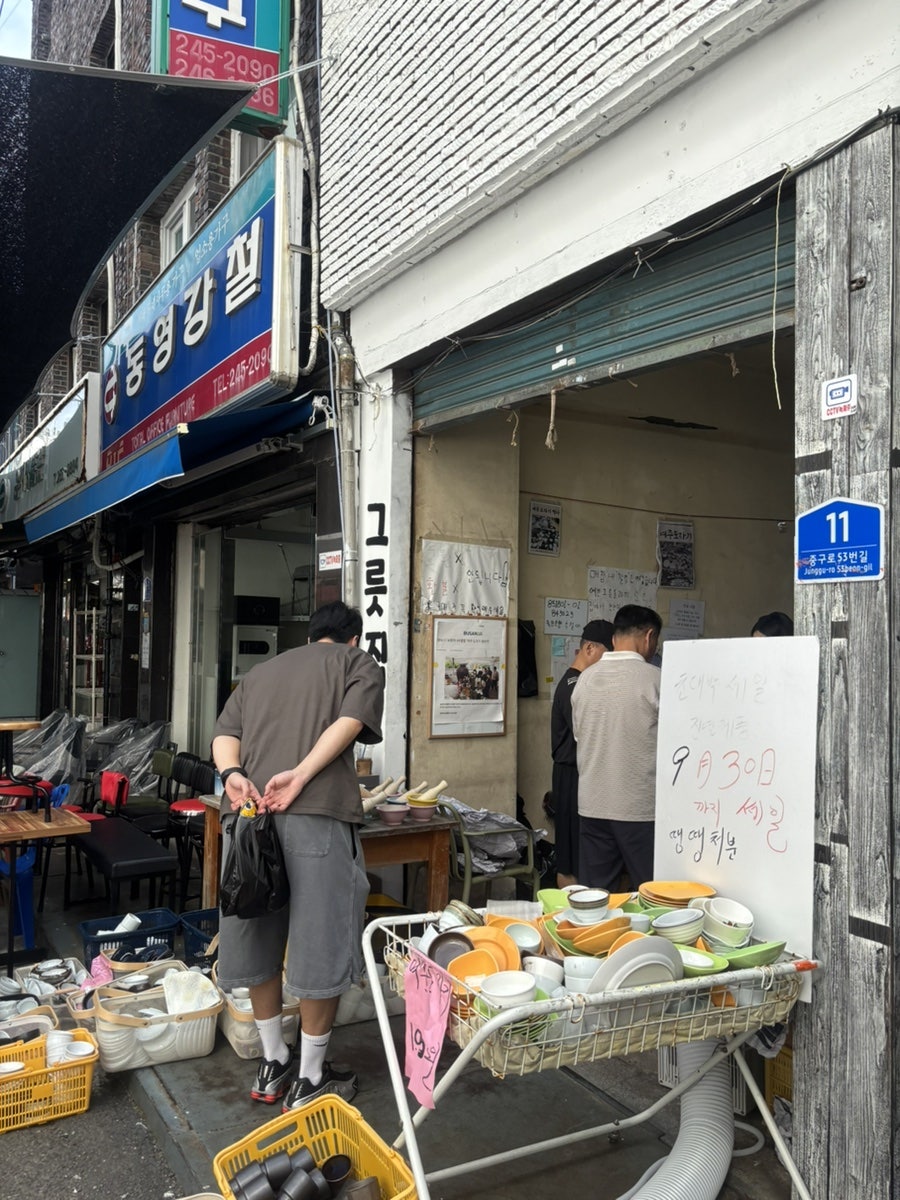 깡통시장 입구 아치형 간판과, 그릇과 생활잡화를 수레에 쌓아 놓은 거리 풍경입니다. 전쟁통에 임시로 선 시장이 지금은 간판 하나로 골목 전체를 대표할 만큼 자리를 잡았습니다.