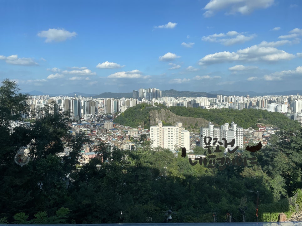 창 너머로 깎여 나간 채석장 바위산과 그 아래 창신동 지붕들, 멀리 서울 도심까지 겹쳐 보입니다. 진열장에는 티라미수와 뉴욕치즈케이크, 스콘이 나란히 놓여 있습니다.