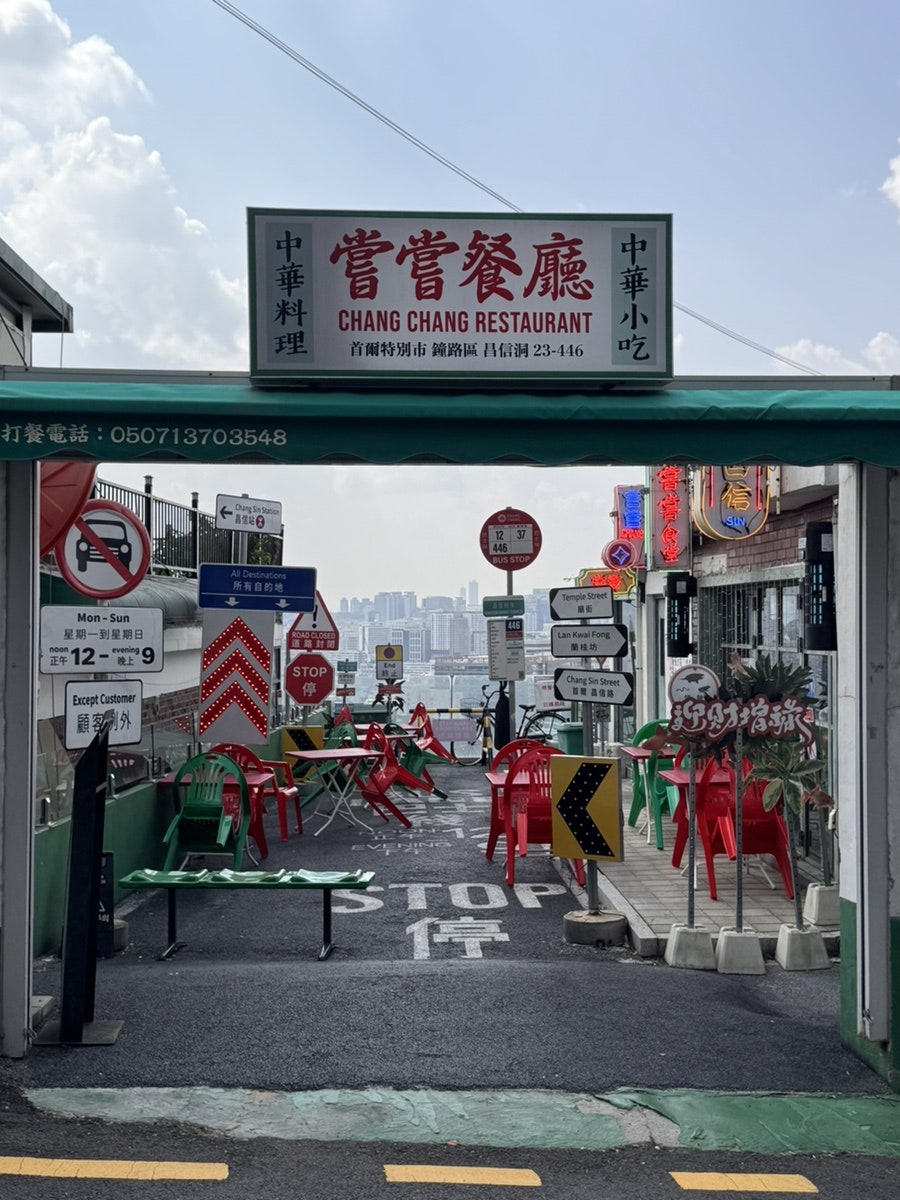 녹슨 철제 셔터 위에 嘗嘗 간판이 걸려 있고, 계단을 다 오르면 Temple Street·Lan Kwai Fong 표지판이 선 옥상 테라스가 나옵니다.