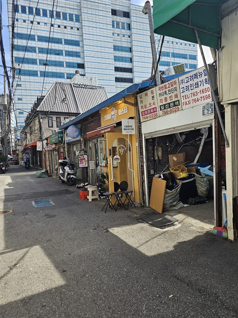 좁은 골목 끝자락, 노란 외벽의 크레페마스터가 보입니다. 창 너머로 주문을 넣는 손님들의 뒷모습도 함께인데,