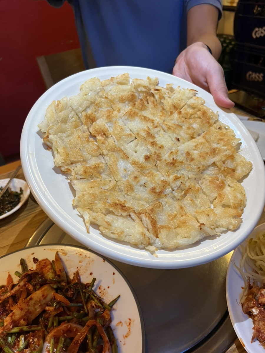 초록 소주병과 맥주병 사이로 매콤하게 무친 해산물 요리가 수북이 쌓여 있고, 갓 구워 낸 감자전을 사장님이 직접 테이블로 가져다주고 있습니다.