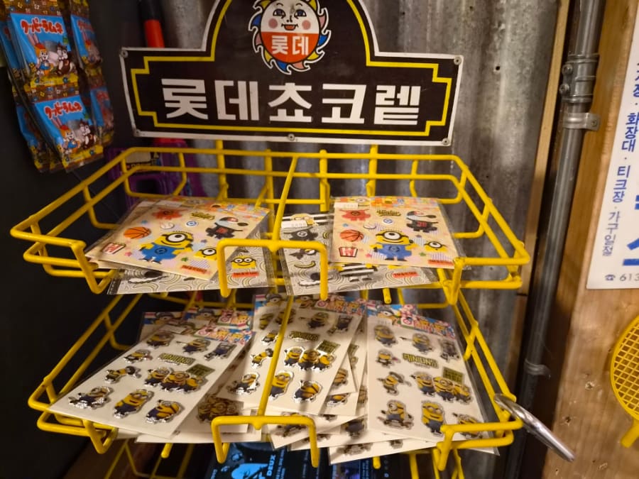 유리 진열장 안에는 콜라병, 양철 로봇, 인형 같은 오래된 장난감들이 켜켜이 놓여 있고, 나무 상자엔 알록달록한 요즘 장난감들이 함께 쌓여 있습니다.