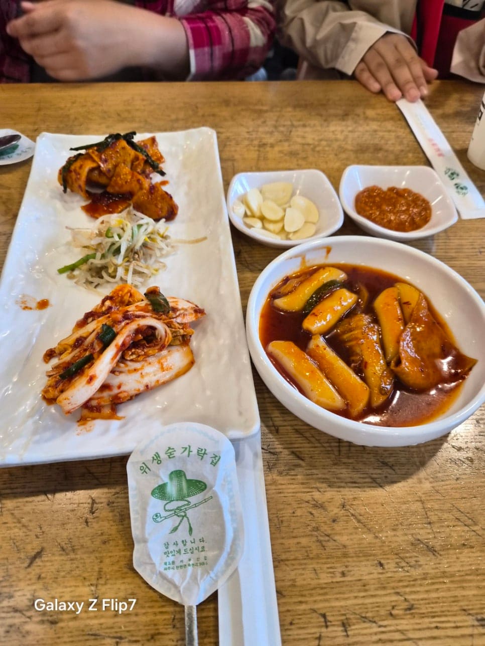 기본으로 나온 밑반찬입니다. 오징어무침, 콩나물, 백김치, 마늘과 양념장, 그리고 매콤한 양념 떡볶이가 함께 놓여 있습니다. 식사가 나오기 전 먼저 상에 오르는 찬입니다.