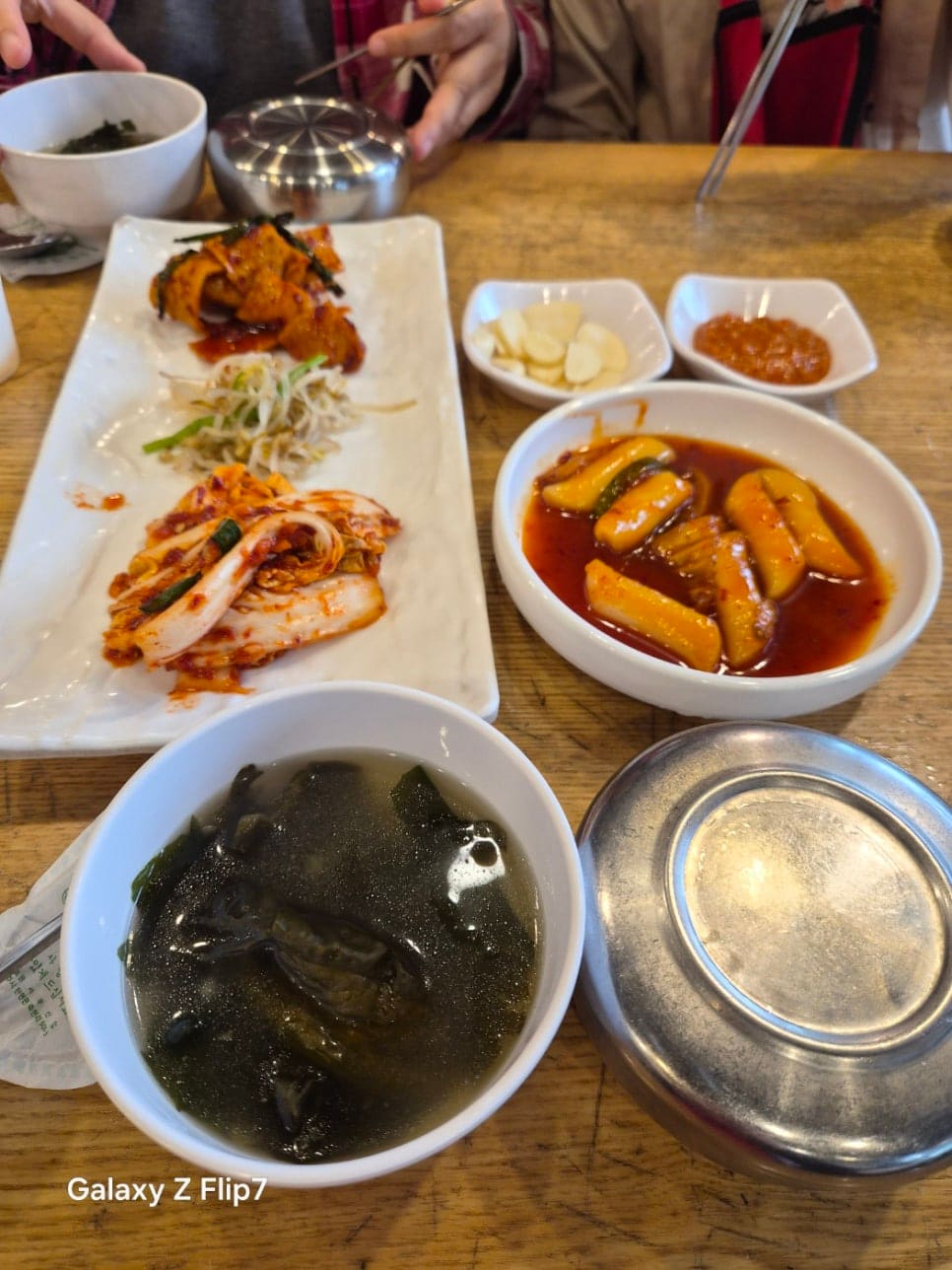 상에 놓인 밑반찬과 미역국입니다. 무말랭이무침, 콩나물, 백김치, 그리고 맑게 끓인 미역국이 함께 놓여 있습니다.