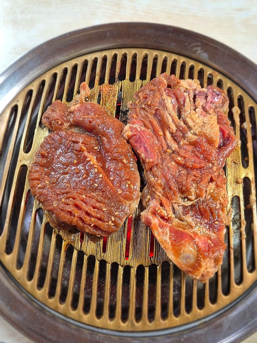 상추와 김치, 깻잎장아찌 같은 밑반찬이 화로를 둘러싸고 있습니다. 황동빛 화로 위에서 돼지갈비 두 덩이가 구워지는데,