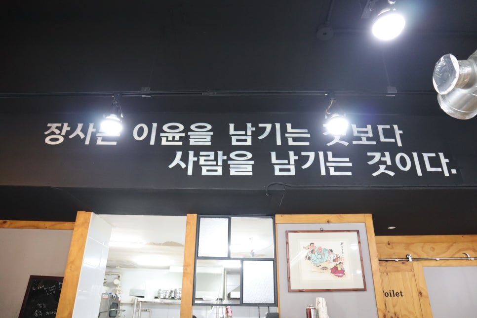 aol4471이 담은 벽면 문구와 내부 테이블입니다. 장사는 사람을 남기는 것이라는 사장님의 철학이 천장 가까이 적혀 있고, 그 아래로 넉넉한 테이블 간격의 홀이 이어집니다.
