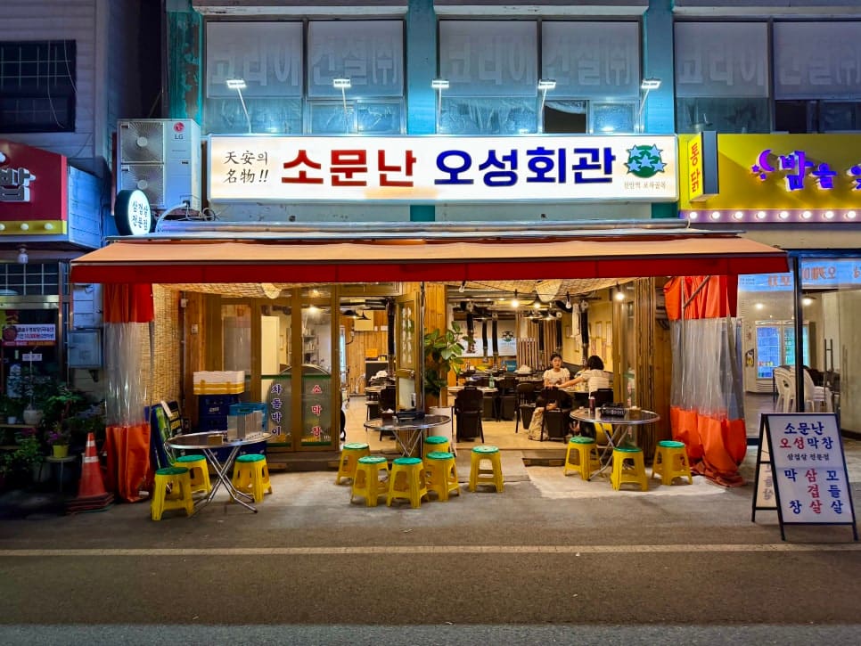 k5727710이 문화로의 포차거리를 찾아 찍은 사진입니다. 노란 플라스틱 의자와 천막 조명이 늘어선 가게 앞으로, 옆 건물의 통닭집 간판까지 이어지는 밤거리가 담겼습니다.