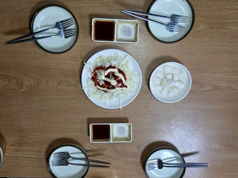 테이블에 놓인 포크와 앞접시들입니다. 소금과 양념소스가 담긴 종지가 두 개씩 놓여 있어, 여럿이 둘러앉아 나눠 먹기 좋은 구성이라는 걸 보여줍니다.