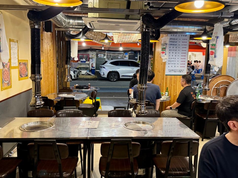 같은 자리에서 가게 안쪽을 보고 찍은 사진입니다. 열린 문 너머로 주차된 차와 맞은편 가게 메뉴판이 보입니다. 실내에 앉아도 거리의 공기가 그대로 들어온다고 적었습니다.