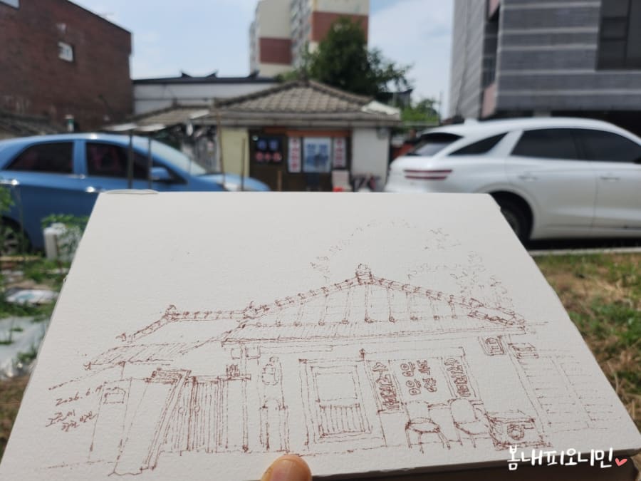 minigmimemo가 찍은 실제 건물과, 같은 자리에서 그린 연필 스케치를 겹쳐 든 모습입니다.