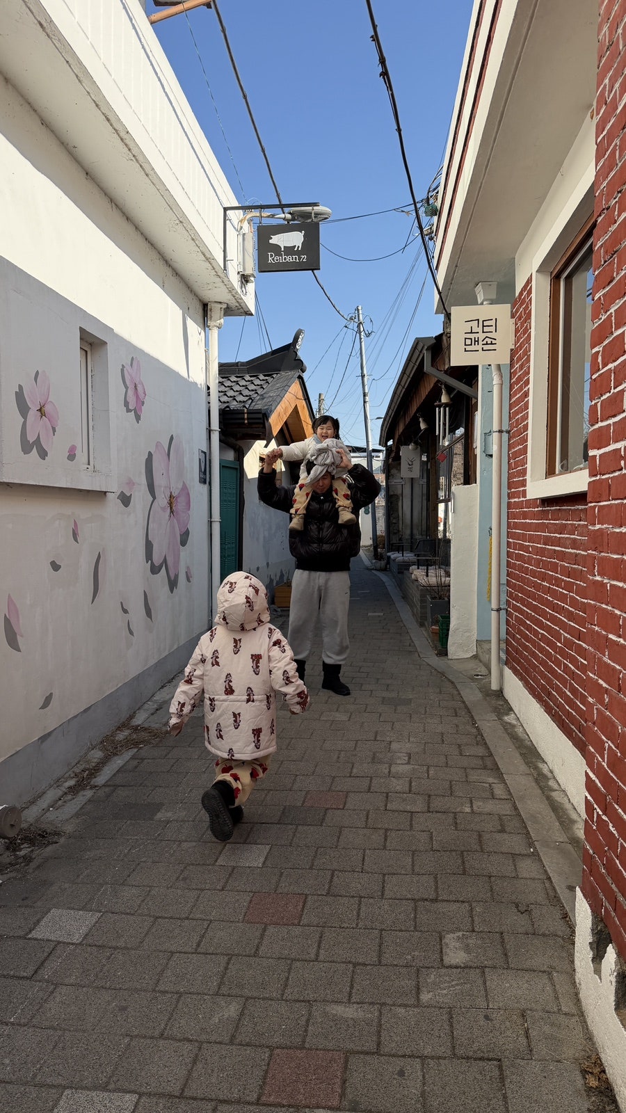 maejunim88이 관아골 골목을 걸으며 찍은 사진입니다. 전깃줄이 낮게 늘어진 좁은 골목과, 가족과 함께 그 길을 걷는 사람들의 뒷모습이 담겼습니다.
