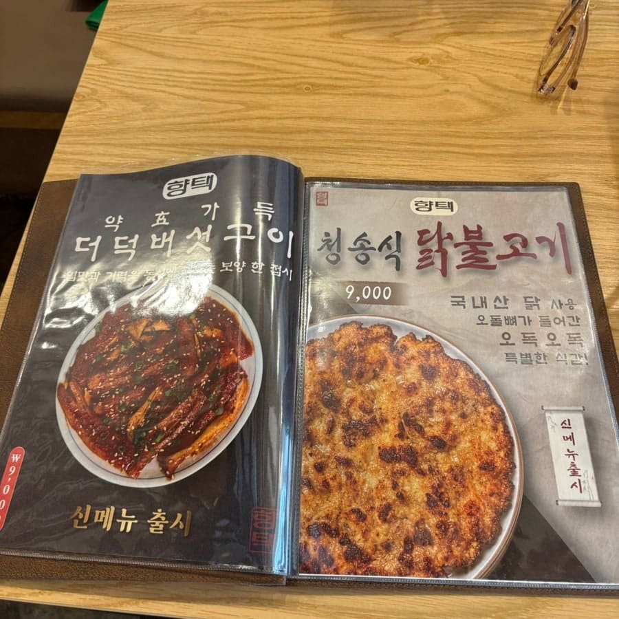 한옥 서까래가 그대로 드러난 입구 쪽 카운터와, 메뉴판에 실린 더덕버섯구이·청송식 닭불고기 사진. 향택이라는 글자가 쓰인 천이 카운터 옆에 걸려 있다.