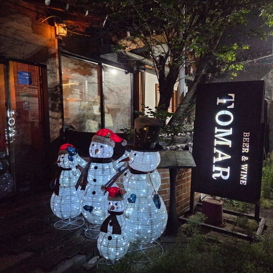 밤이 되면 또마르 입구에 세워둔 눈사람 조명이 켜지고, 안쪽에서는 한옥 서까래 아래로 매달린 알전구와 맥주 탭이 은은하게 빛난다.