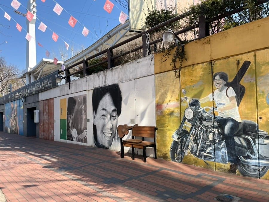 wshooooooooo가 촬영한 낮의 골목입니다. 벽화가 그려진 담과 벤치, 그리고 기타 모양 벤치에 걸터앉은 아이의 모습에서 이 골목을 걷는 낮 시간의 공기가 느껴집니다.