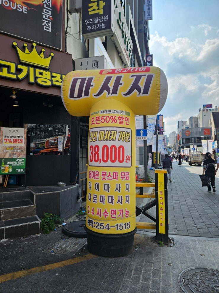qwer67415가 남긴 사진입니다. 오락실과 카페 간판이 늘어선 낮의 으능정이거리를 지나, 고기명작 건물 앞 대형 풍선 입간판까지 걸어가는 길을 담았습니다.