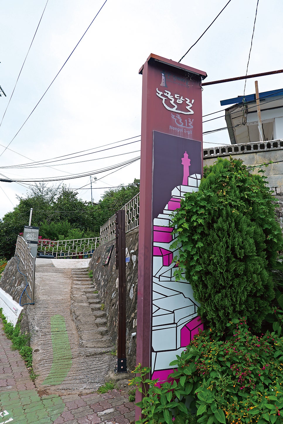 dica1234가 담은 논골1길 입구입니다. 바랜 보랏빛 표지판과 가파른 돌계단, 그리고 묵호등대·바람의언덕까지 거리를 알려주는 방향 표지판이 이 골목의 첫인상을 보여줍니다.