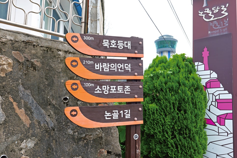 dica1234가 담은 논골1길 입구입니다. 바랜 보랏빛 표지판과 가파른 돌계단, 그리고 묵호등대·바람의언덕까지 거리를 알려주는 방향 표지판이 이 골목의 첫인상을 보여줍니다.