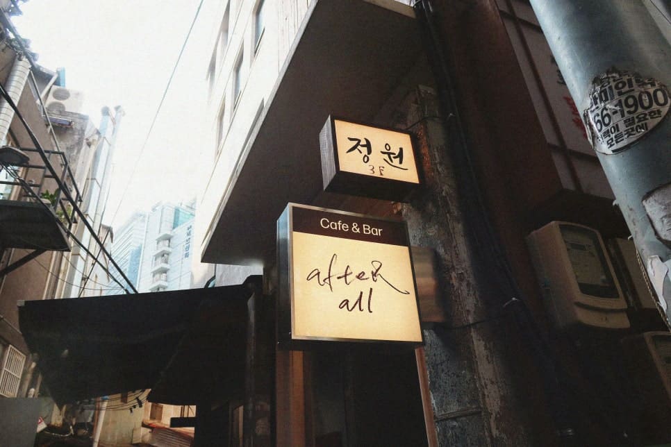 어두운 건물 벽면에 "Cafe & Bar after all"이라는 간판이 조명에 비춰있다. 골목 깊숙이 숨어있는 카페의 입구를 알려주는 작은 네온사인.
