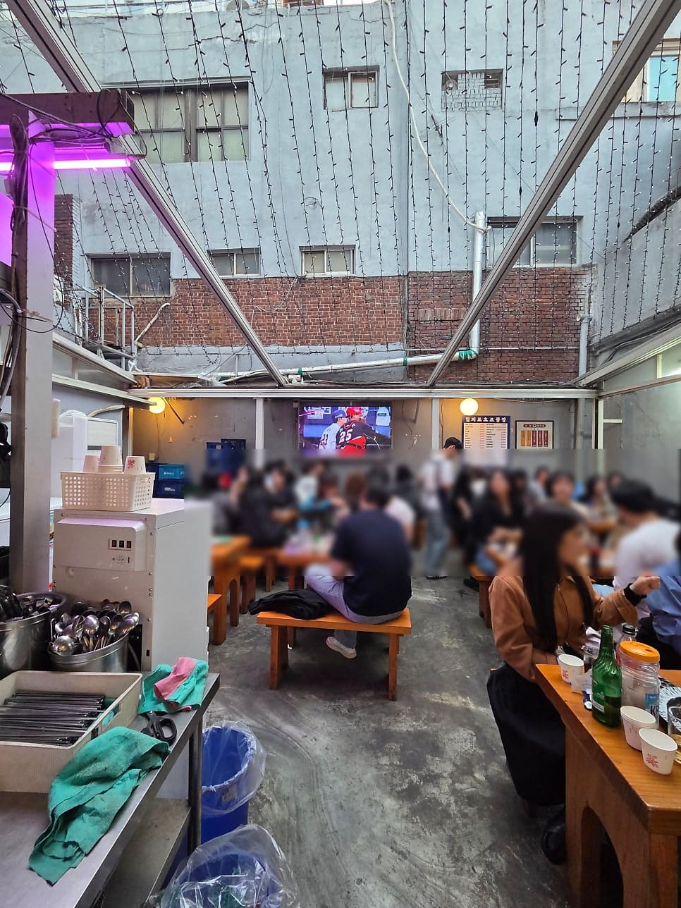 천막 지붕 아래 평상 자리마다 사람이 가득 찼습니다. 벽에 걸린 TV로 야구 중계를 보며 잔을 부딪치는 모습이, 을지로 야장의 흔한 저녁 풍경이라고 블로거는 적었습니다.