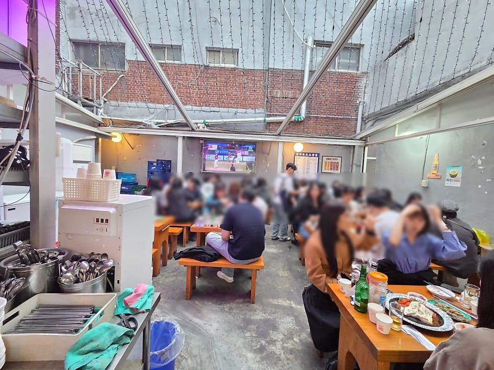 천막 지붕 아래 평상 자리마다 사람이 가득 찼습니다. 벽에 걸린 TV로 야구 중계를 보며 잔을 부딪치는 모습이, 을지로 야장의 흔한 저녁 풍경이라고 블로거는 적었습니다.