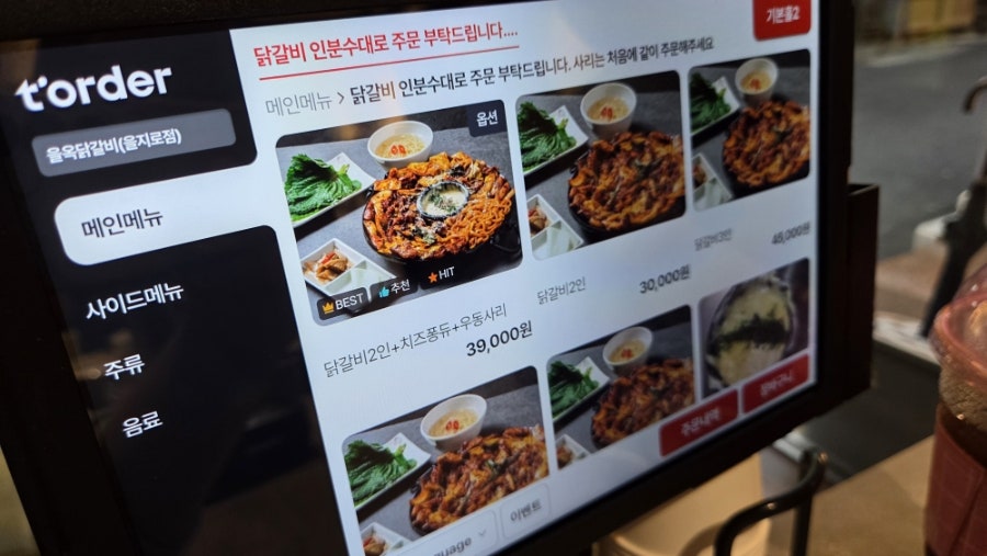 dh11188은 주문 전 키오스크 화면과, 다 볶여 나온 닭갈비 판을 함께 찍었습니다. 화면에는 '닭갈비 2인+치즈퐁듀+우동사리 39,000원'이라고 적혀 있고,
