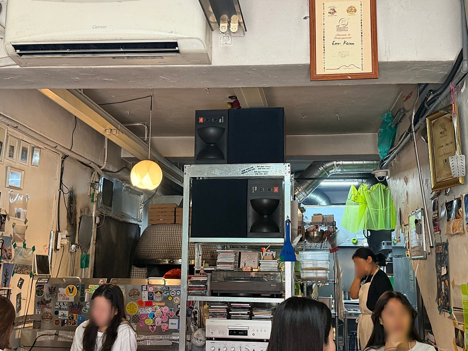 han4869은 빼곡히 붙은 옛날 사진과 상패, 손글씨 메모로 가득한 벽, 그리고 화덕과 스피커, 음반 더미가 좁은 공간에 뒤섞인 전경을 찍었습니다.