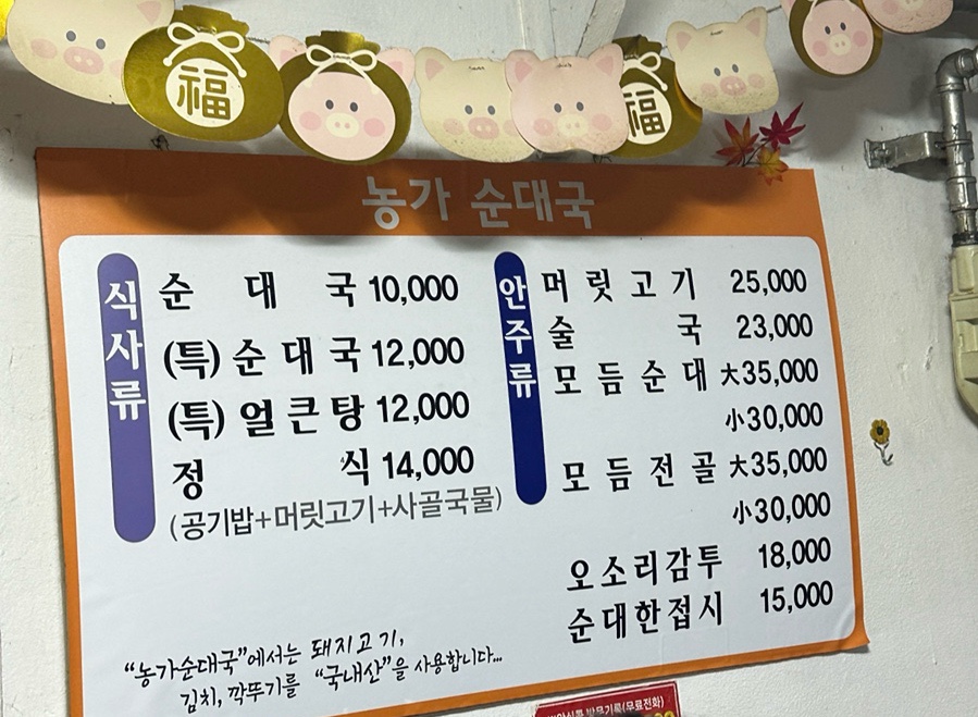 tigung1107은 큰 국솥과 플라스틱 간이 의자가 늘어선 가게 앞, 그리고 돼지 캐릭터 장식 아래 붙은 메뉴판을 찍었습니다.