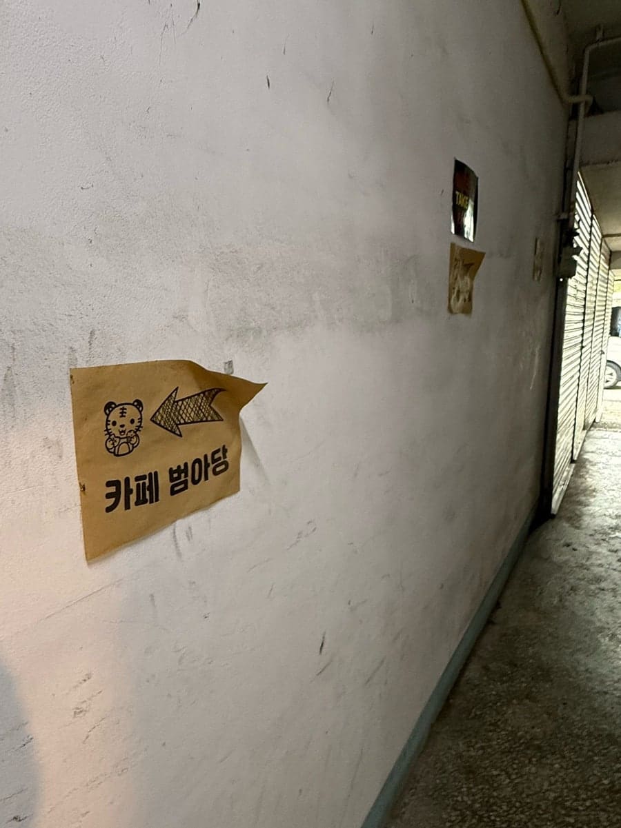 dkfla7522이 찾아가는 길에 찍은 사진입니다. 범환멘션 상가의 좁고 낡은 통로를 지나면, 벽에 붙은 호랑이 캐릭터 화살표가 '카페 범아당' 방향을 가리킵니다.