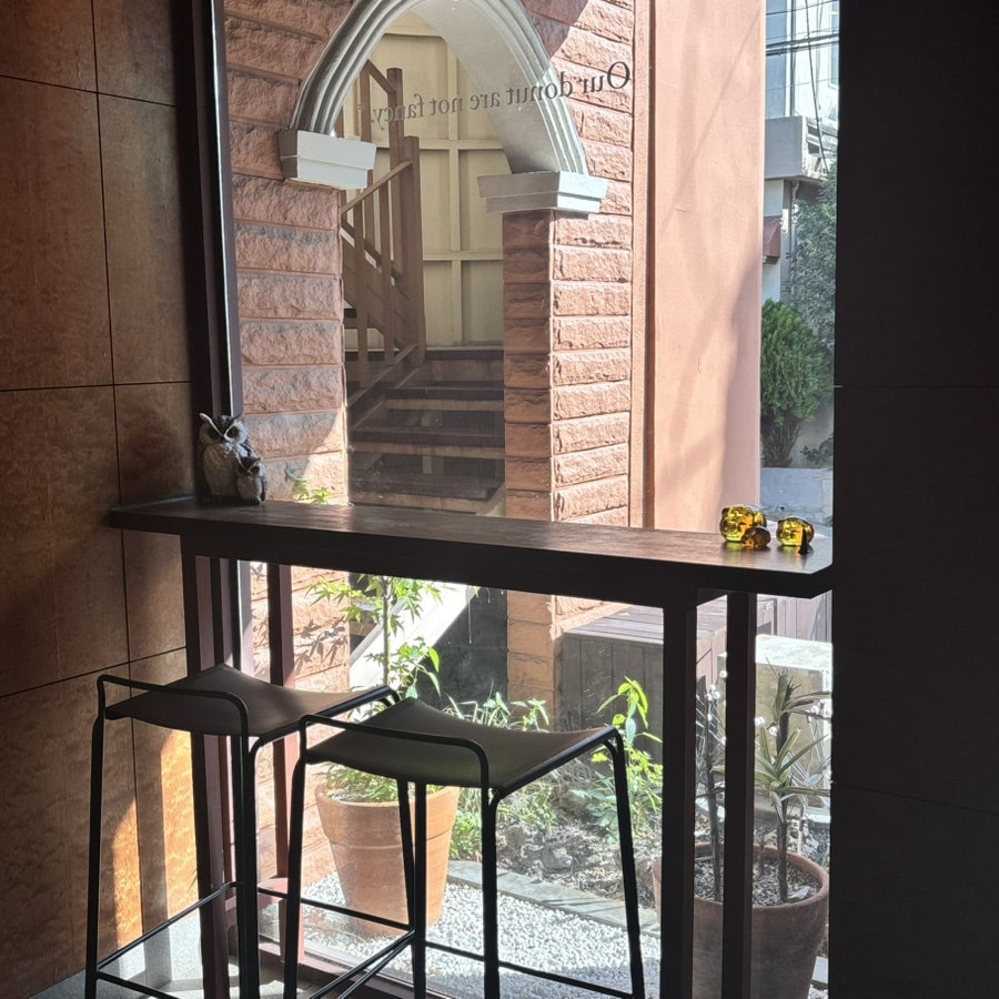 hhvely2가 담은 창가 자리입니다. 둥근 테이블과 의자 너머로 바깥 테라스의 억새와 화분이 보이고, 다른 자리에서는 아치형 벽돌 계단이 창밖으로 내다보입니다.
